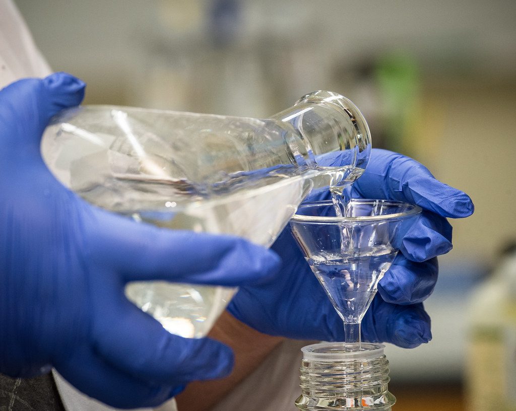 Gloved hands pouring liquid in a laboratory
