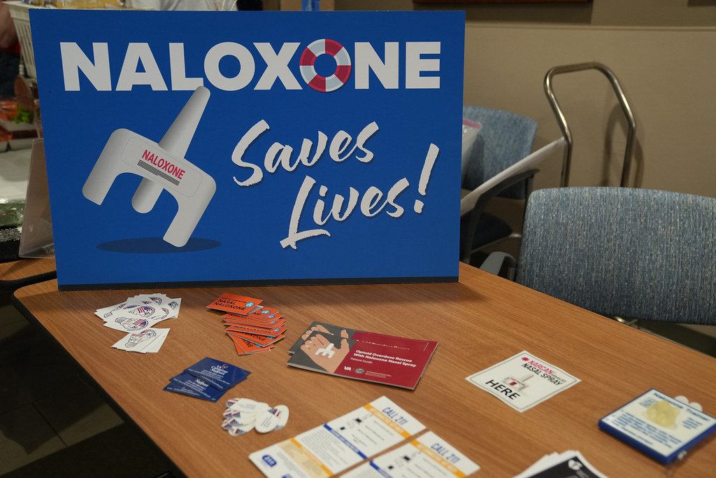 Naloxone kits on a table under a sign reading Naloxone Saves Lives