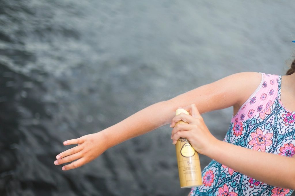 A child spraying sunscreen on an arm